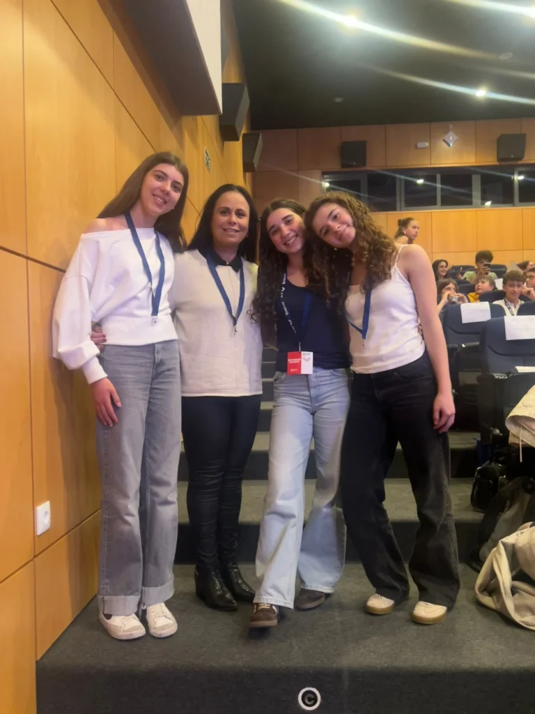 Quatro jovens e uma adulta com cordões ao pescoço posam num auditório, durante a Sessão Distrital do Parlamento dos Jovens.