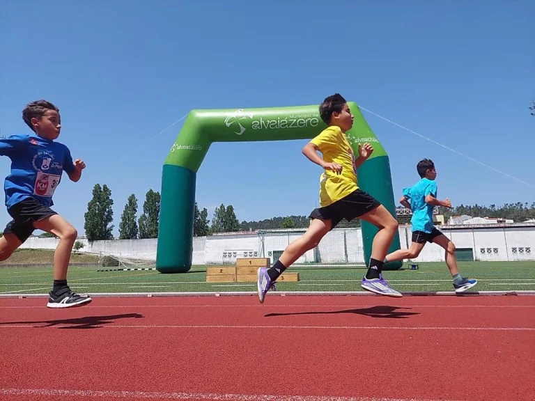 Três alunos a correr numa pista de atletismo, junto a um arco insuflável verde do Município de Alvaiázere.