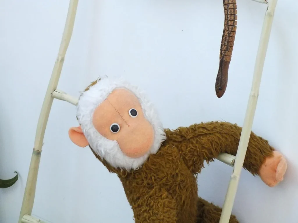 Macaco de peluche castanho, com cabeça de pelo branco, agarrado a uma escada de bambu.