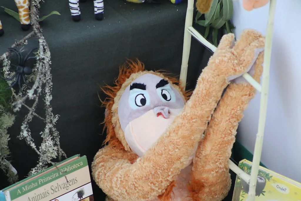 Peluche de orangotango alaranjado a subir uma escada de canas, ao lado do livro «Animais Selvagens».