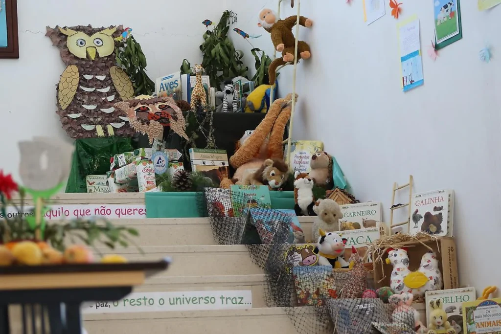 Degraus com peluches de animais da quinta (galinha, vaca, carneiro, coelho), livros e cartazes com frases.
