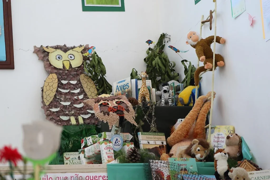 Canto da exposição com uma coruja de cartolina, peluches de macaco e leão e livros sobre aves e animais selvagens.
