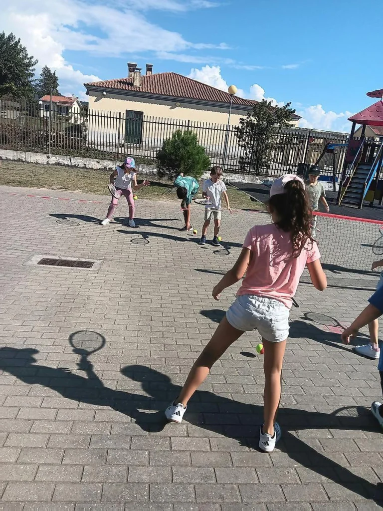Alunos a jogar ténis com raquetes e bolas no recreio do Centro Escolar de Avelar, com a rede ao fundo.